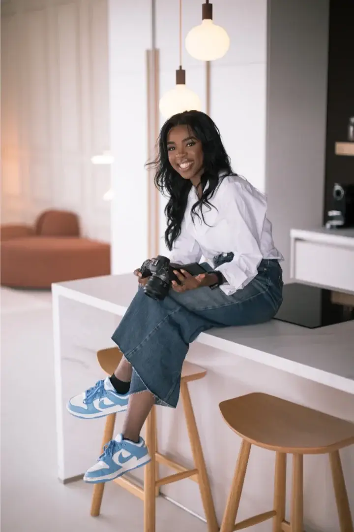 Amazonia Monguya sitting on a kitchen island holding a camera, photographed in a modern interior for Refined Studios.